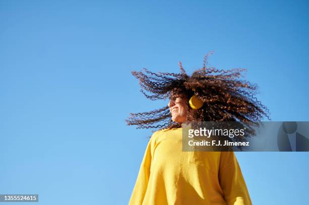 woman moving her curly hair with blue sky in the background - kinky stock-fotos und bilder
