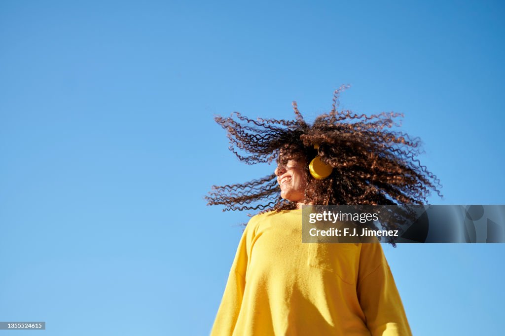 Woman moving her curly hair with blue sky in the background