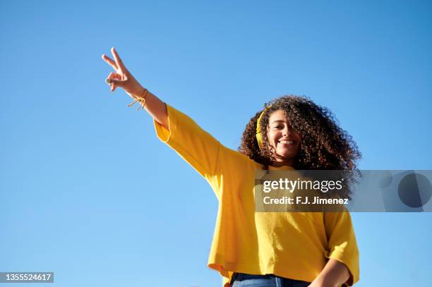 portrait of woman with triumph gesture with blue sky in the background - siegerpose stock-fotos und bilder