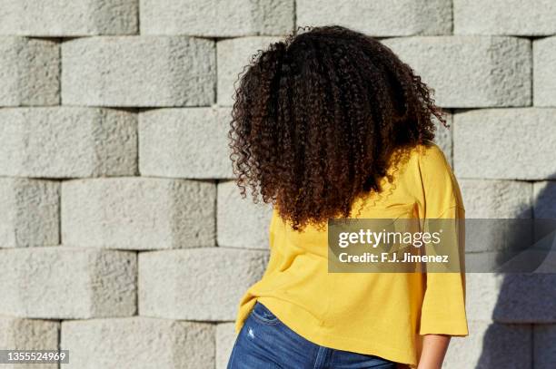 woman showing hair in front of stone wall - afro frisur stock-fotos und bilder