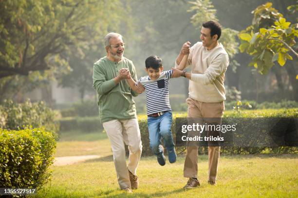 senior man with adult son carrying grandson by hands at park - grandpa son stock pictures, royalty-free photos & images