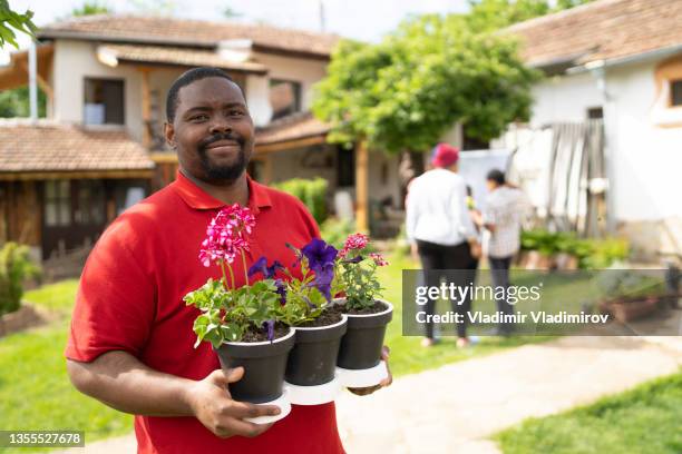 un hombre sonriendo a la cámara sosteniendo tres macetas de flores - man flower shirt fotografías e imágenes de stock