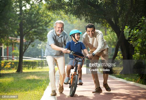 boy learning bicycle with father and grandfather at park - learning generation parent child stock pictures, royalty-free photos & images