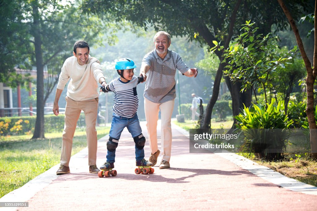 Boy learning roller skating with father and grandfather at park