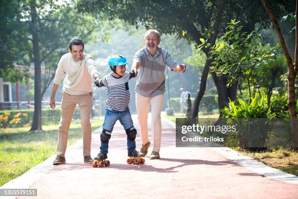 boy learning roller skating with father and grandfather at park - kneepad stock pictures, royalty-free photos & images