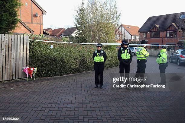 Floral tributes lay next to police guarding the scene near a house in Pudsey where four bodies were discovered on December 12, 2011 in Leeds,...