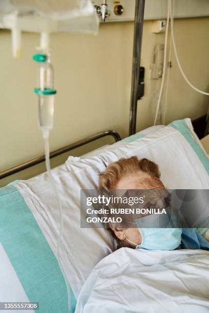 senior woman wearing mask infected by coronavirus on hospital bed receiving cancer medicine treatment by drip. vertical photo - receiving treatment concerned stock pictures, royalty-free photos & images