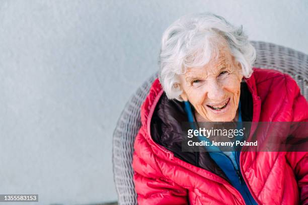 cheerful 100-year-old elderly senior caucasian woman sitting and laughing outdoors in the winter - 101 stockfoto's en -beelden