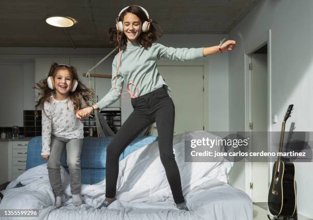 girls sisters listening to music and jumping on the sofa, naughty - sister stock photos et images de collection