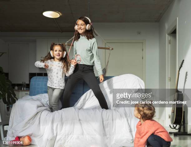 sisters girls listening to music and jumping on the sofa - best song stock pictures, royalty-free photos & images
