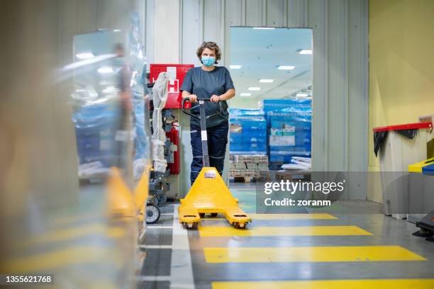 warehouse worker pushing pallet truck in storage room - megawinkel stockfoto's en -beelden