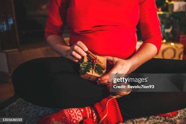 happy pregnant woman wrapping gifts near the fireplace - woman ribbon happy stockfoto's en -beelden