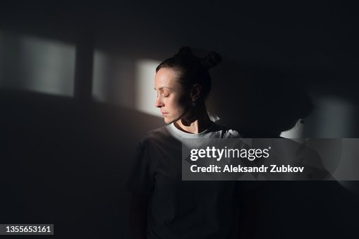 A lonely Young Sad Calm Girl Or Woman stands against a white wall, in a psychiatric clinic or at home, in the rays of sunlight, with her eyes closed. The Concept of Depression from Illness and Quarantine, Fatigue and Impotence. A copy of the space. A lonely Young Sad Calm Girl Or Woman stands against a white wall, in a psychiatric clinic or at home, in the rays of sunlight, with her eyes closed. The Concept of Depression from Illness and Quarantine, Fatigue and Impotence. A copy of the space.