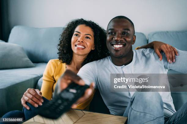 cute young couple cuddling while watching tv. - african american watching tv stock pictures, royalty-free photos & images