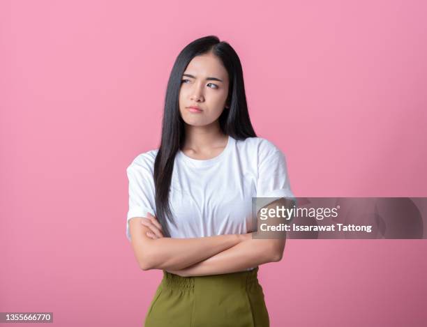 portrait of an upset young casual girl standing with arms folded isolated over pink background - grumpy stockfoto's en -beelden