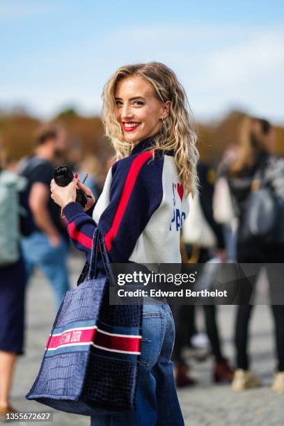 Guest wears gold and silver earrings, a navy blue mesh with polka dots shirt from Dior, a white latte / navy blue and red stripes zipper pullover...