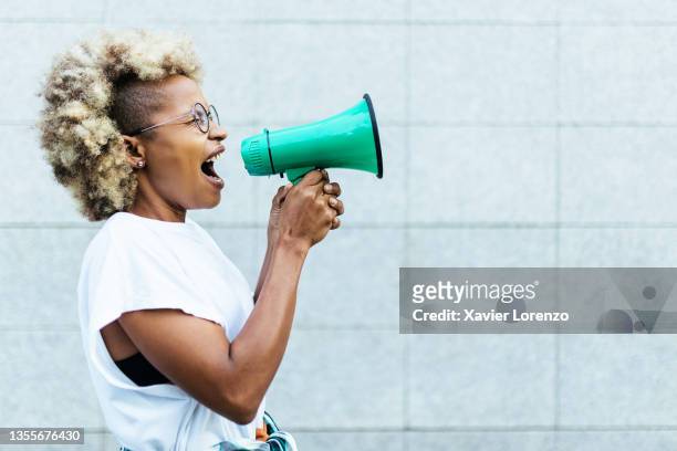 hispanic latin young adult woman shouting through a megaphone outdoors - megaphone stock pictures, royalty-free photos & images