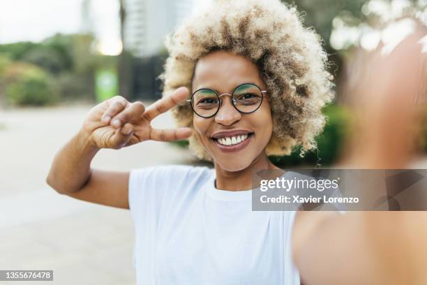 african american woman making peace sign and smiling while taking a selfie outdoors on the street. - victory sign stock-fotos und bilder
