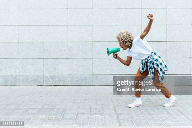 angry woman yelling on megaphone while protesting about something outdoors on the street. - protests stock-fotos und bilder