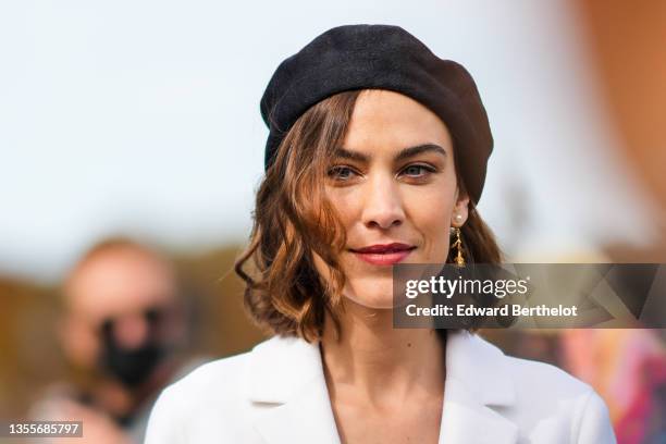 Alexa Chung wears a black wool beret / hat, gold earrings, a white long blazer jacket, outside the Dior show, during Paris Fashion Week - Womenswear...