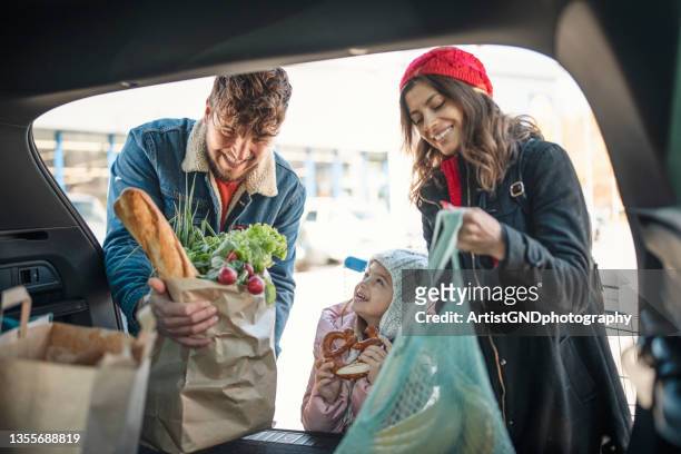 süße familie, die lebensmittel im kofferraum verlädt - couple in supermarket stock-fotos und bilder