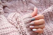 Women's hands with a beautiful matte oval manicure in a warm knitted sweater. Winter trend, polish beige nails with gel polish, shellac. Copy space.
