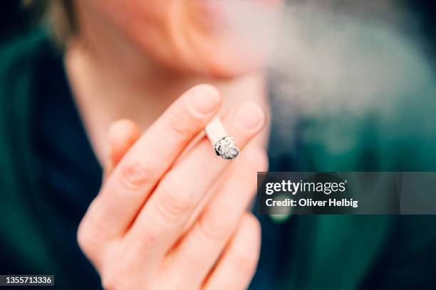 unrecognizable woman wrapped in cigarette smoke holding a lit cigarette in her hand - e cig foto e immagini stock