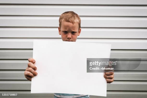 a frowning little boy holds a blank placard for copying the text - small placard stock pictures, royalty-free photos & images