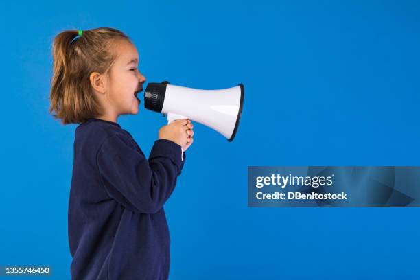 little blond hair girl wearing blue sweatshirt, yelling and speaking through a white megaphone, on light blue background. - girl with blue hair stock pictures, royalty-free photos & images