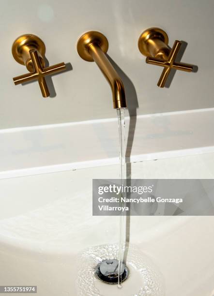 hot and cold water flowing from a  gold coloured stainless steel faucet - haushaltsarmatur stock-fotos und bilder