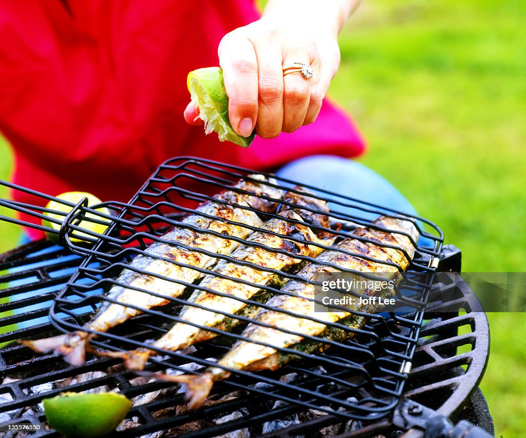 Lime being squeezed over mackerel on barbecue