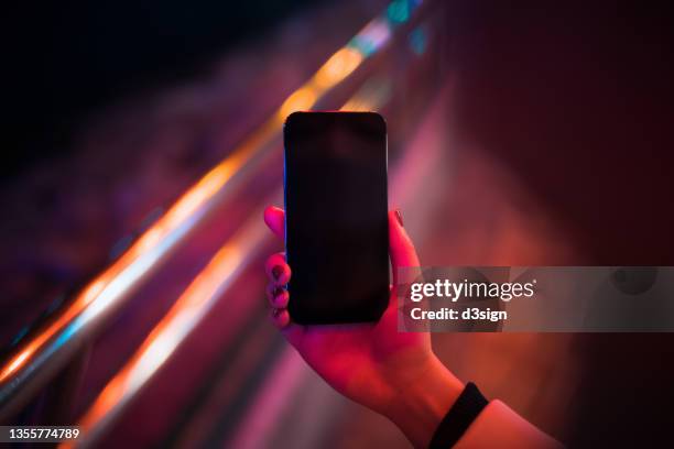 a woman lit by red neon coloured lights and close up of her hand using smartphone in downtown prosperous city street at night. smartphone with blank screen for design mockup - human hand foto e immagini stock