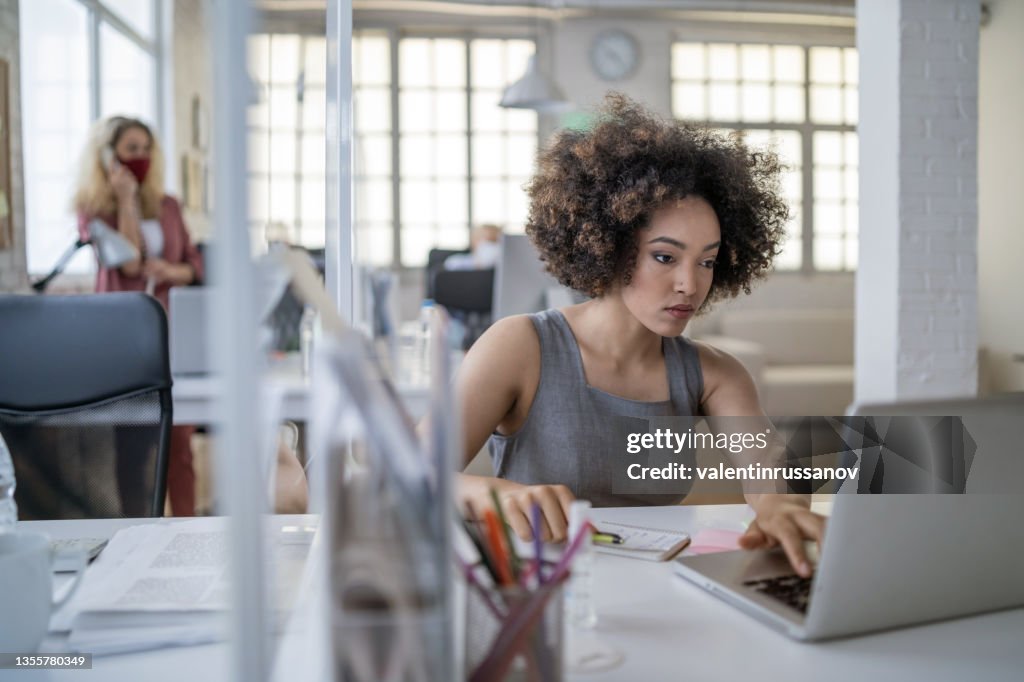 Afroamerikanische Fachfrau, die nach dem Covid-Lockdown in einem modernen Büro an einem Laptop arbeitet.