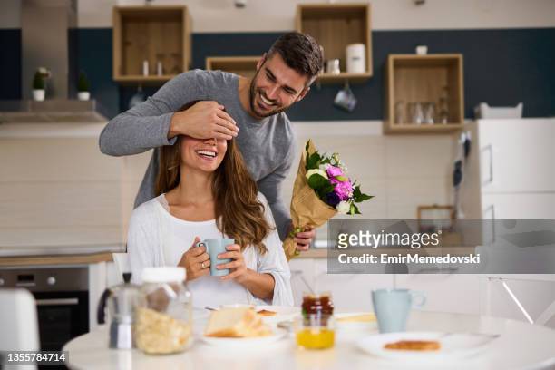 uomo che tiene la mano sugli occhi della moglie prima di sorprenderla con un mazzo di fiori a casa - man giving flowers foto e immagini stock
