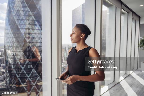 contemplative british businesswoman standing at window - black woman looking at view stock pictures, royalty-free photos & images