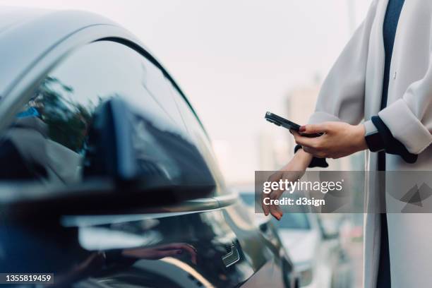 close up of young asian woman using mobile app device on smartphone to unlock the doors of her intelligence car in city street. wireless and modern technology concept - car keys hand foto e immagini stock