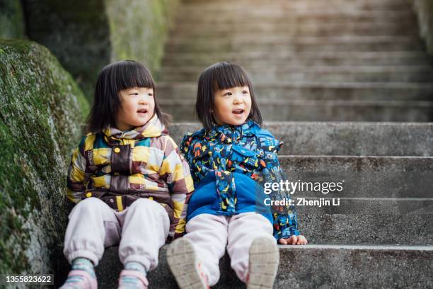 3 year twin sisters sitting on staircase side by side looking up - asian twins photos et images de collection