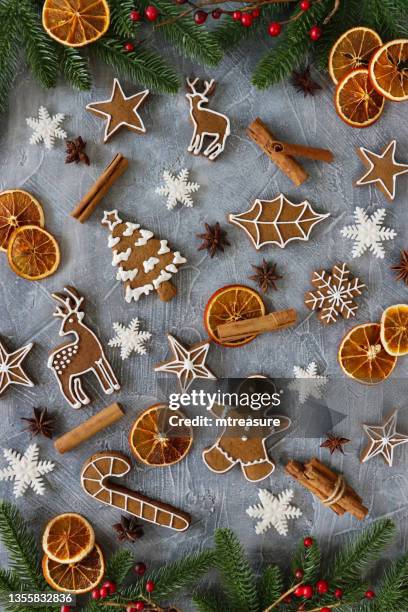 image of festive christmas design poster, homemade gingerbread biscuit cutout shapes of christmas trees, candy canes, bells, holly leaves, snowflakes, reindeer, stars and gingerbread men cookies, spruce needles and red berries border on grey background - gingerbread men stockfoto's en -beelden