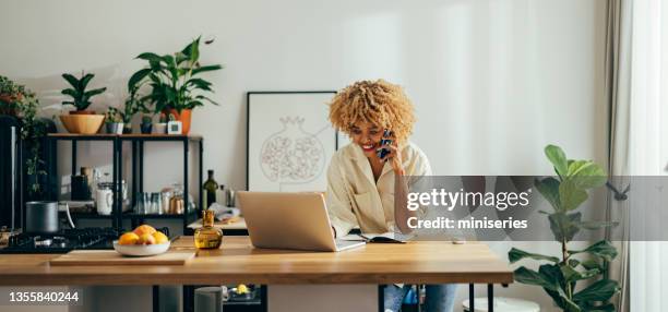 beautiful cheerful woman having a phone call while working on a laptop - using laptop at home happy copy space stock pictures, royalty-free photos & images
