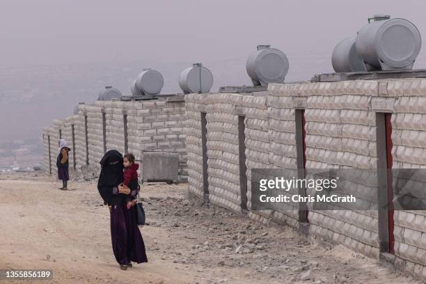 Displaced Syrian woman walks with her child past newly construct brick housing inside the Kefer Losing camp run by the Turkish Red Crescent on the...