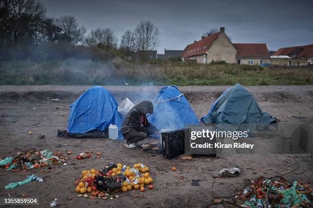 Refugee sits by a fire to keep warm at daybreak at camp on the outskirts of Calais on November 27, 2021 in Calais, France. There currently around...