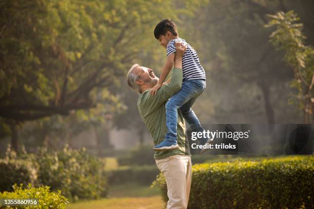 senior man lifting up his grandson at park - indian grandparents stock pictures, royalty-free photos & images