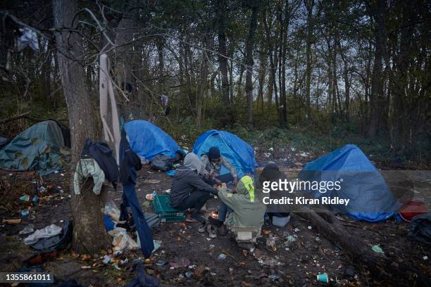 Refugees from Sudan sit by a fire to keep warm at a camp in a small woods on the outskirts of Calais on November 27, 2021 in Calais, France. There...