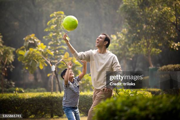 father and son having fun while playing with ball at park - father and son park stock pictures, royalty-free photos & images