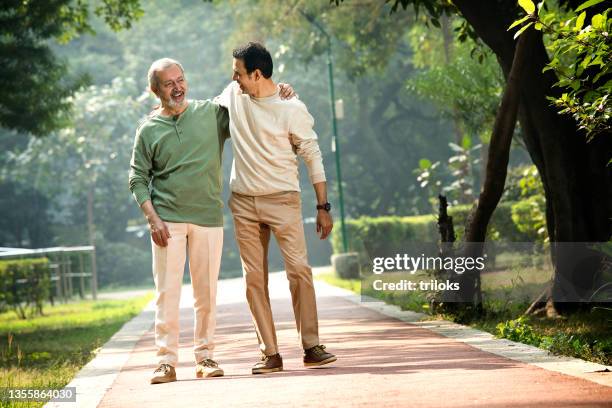 happy senior man walking with son at park - happy adult stock pictures, royalty-free photos & images