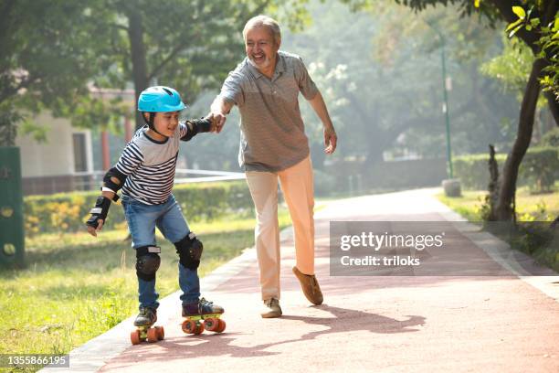 grandfather assisting his grandson skating at park - padding stock pictures, royalty-free photos & images