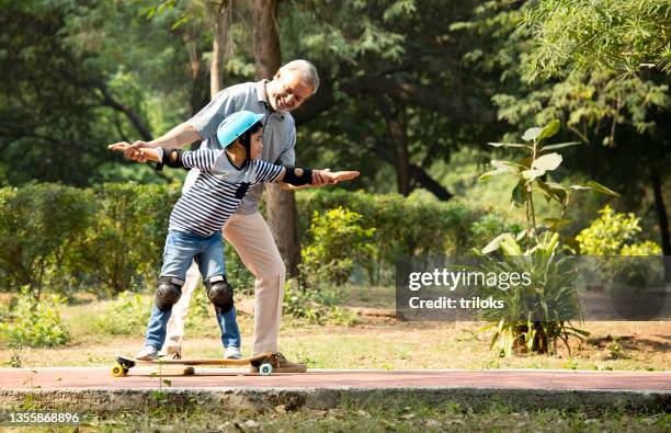 boy in protective sportswear learning skateboarding with grand father at park - skateboard park imagens e fotografias de stock