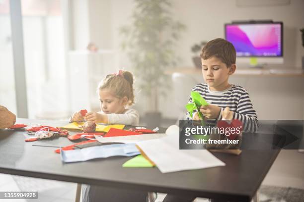 little brother and sister making christmas gifts from paper at home - child cutting card stock pictures, royalty-free photos & images