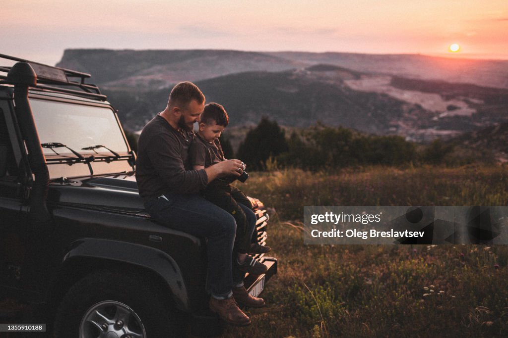 Father teaching son to photograph on old film photo camera outdoors at sunset