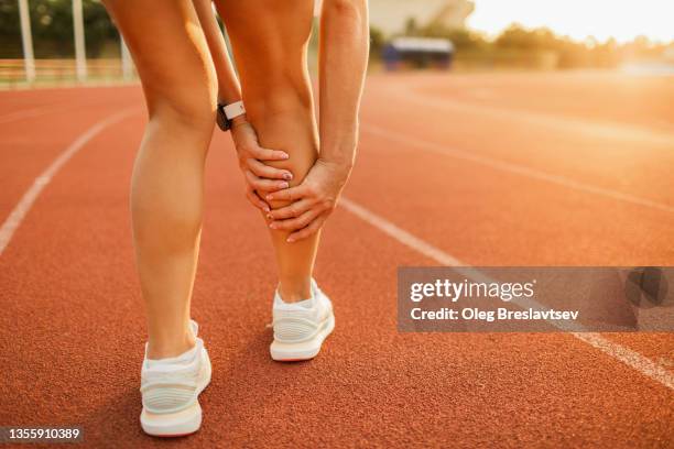 running injury, health problems in sport. hands holding spasmed calf or achilles muscle on sports track - female muscle calves stock pictures, royalty-free photos & images